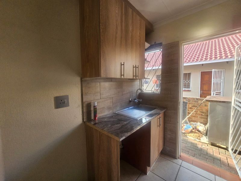 A compact scullery area featuring wood-look cabinetry, a stainless steel sink, and direct access to an outdoor paved courtyard.