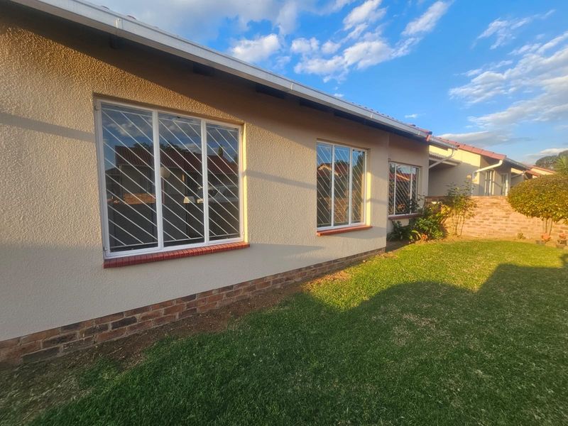 A view of the rear exterior of the townhouse featuring a well-maintained lawn, brick plinth detailing, and windows fitted with security bars.