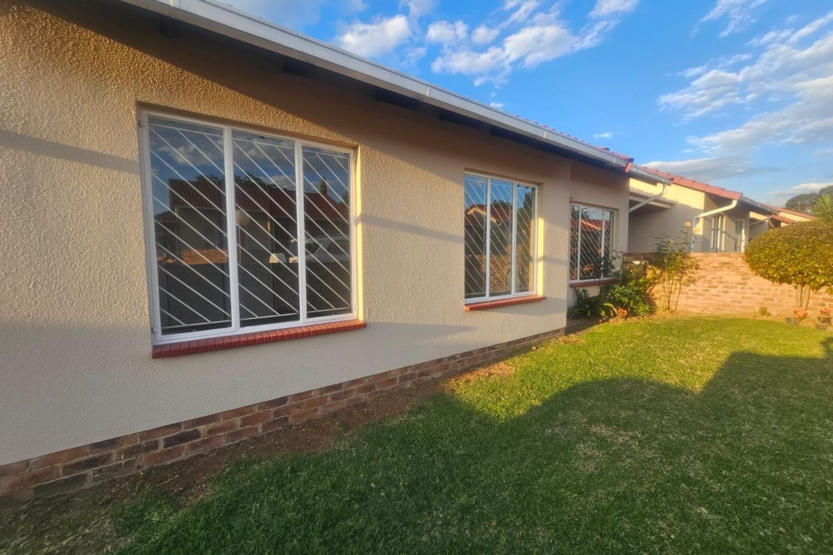 A view of the rear exterior of the townhouse featuring a well-maintained lawn, brick plinth detailing, and windows fitted with security bars.