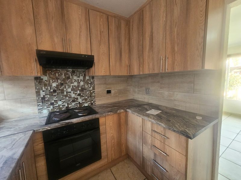 Modern kitchen featuring wood-look cabinetry, stone-effect countertops, built-in oven with extractor fan, and a decorative mosaic tile backsplash.