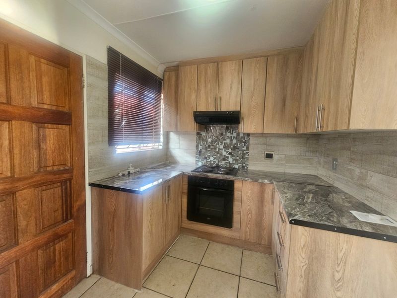 A functional kitchen featuring wood-look cabinetry, stone-effect countertops, a built-in oven with hob, and a mosaic tile backsplash.