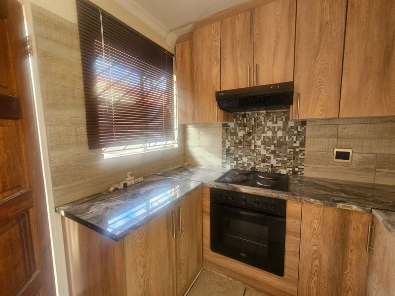 A compact, well-maintained kitchen featuring wood-look cabinetry, marble-effect countertops, a mosaic tile backsplash, and integrated electric oven and hob.