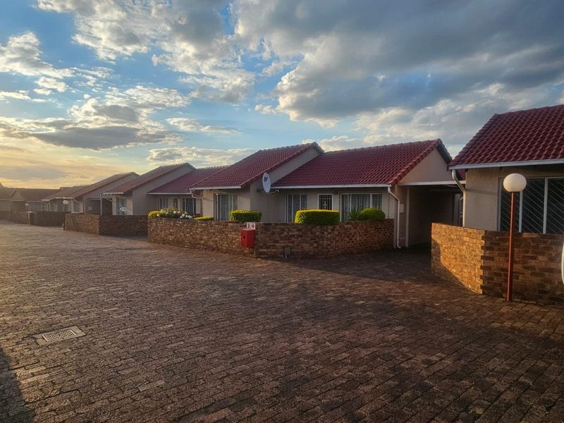 A view of the townhouse complex exterior featuring paved driveways, facebrick boundary walls, and tiled roofing under a clear sky.