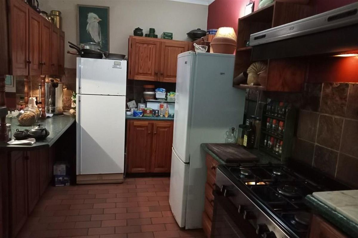 A traditional kitchen featuring wooden cabinetry, a gas stove with extractor fan, and tiled flooring, offering a functional layout with ample storage space.