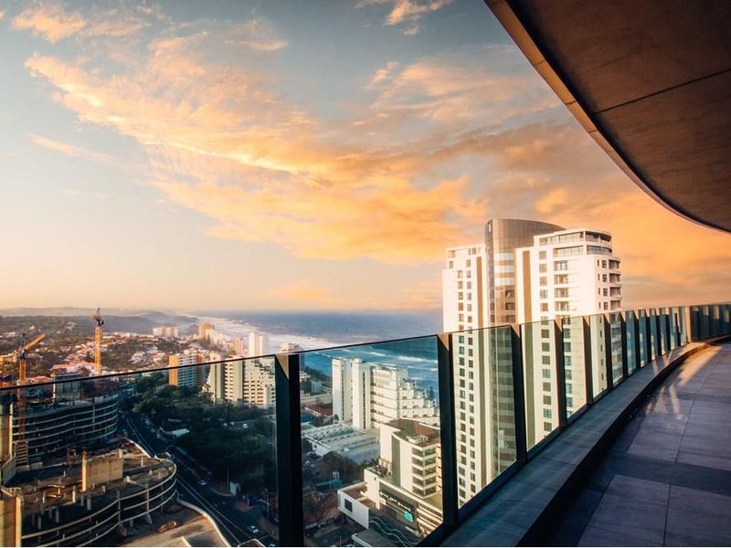 Spacious penthouse balcony featuring a modern glass balustrade and tiled flooring, offering expansive panoramic views of the coastline and city skyline.