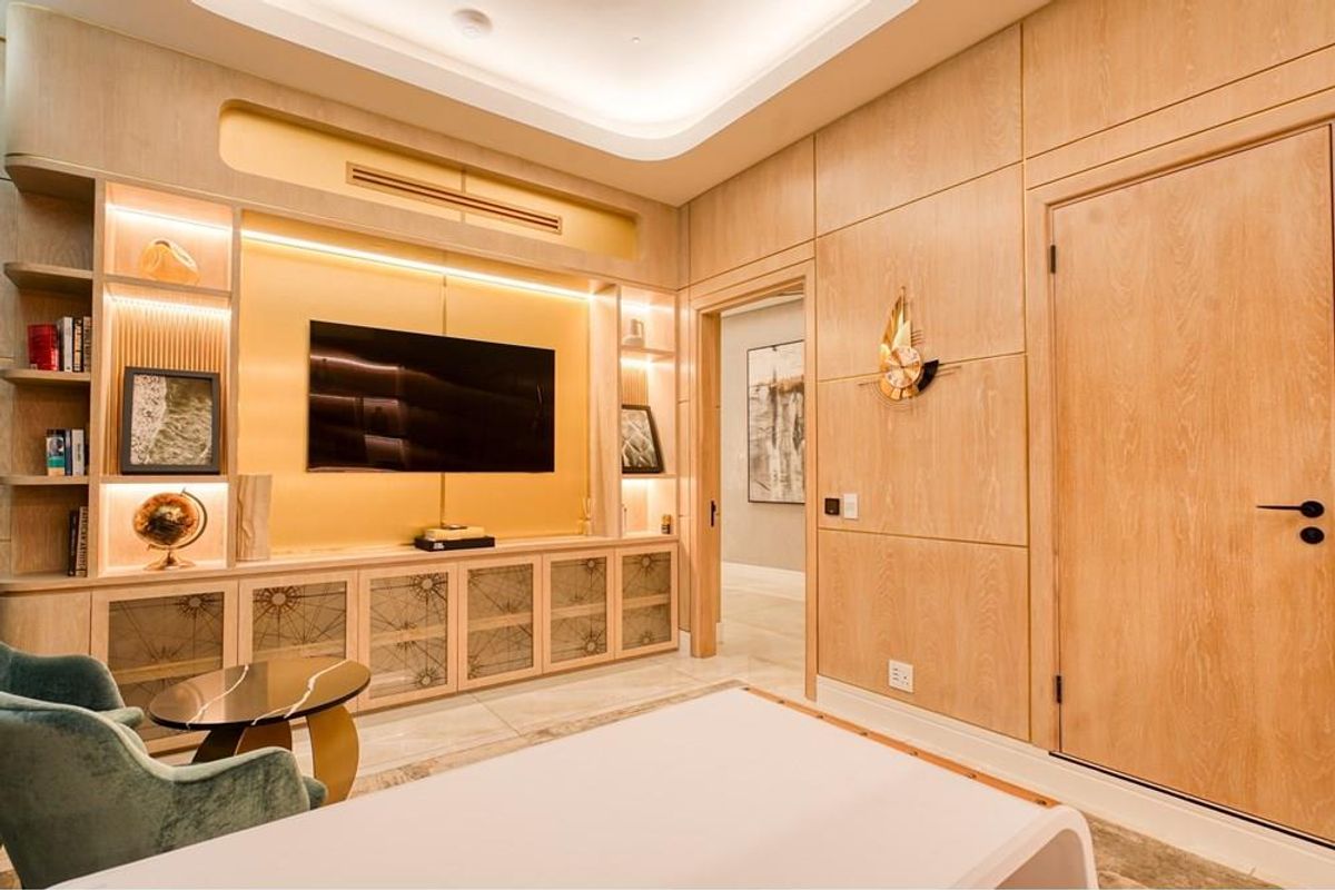 A sophisticated living room featuring custom light wood built-in cabinetry, integrated display shelving, recessed cove lighting, and high-quality marble flooring.