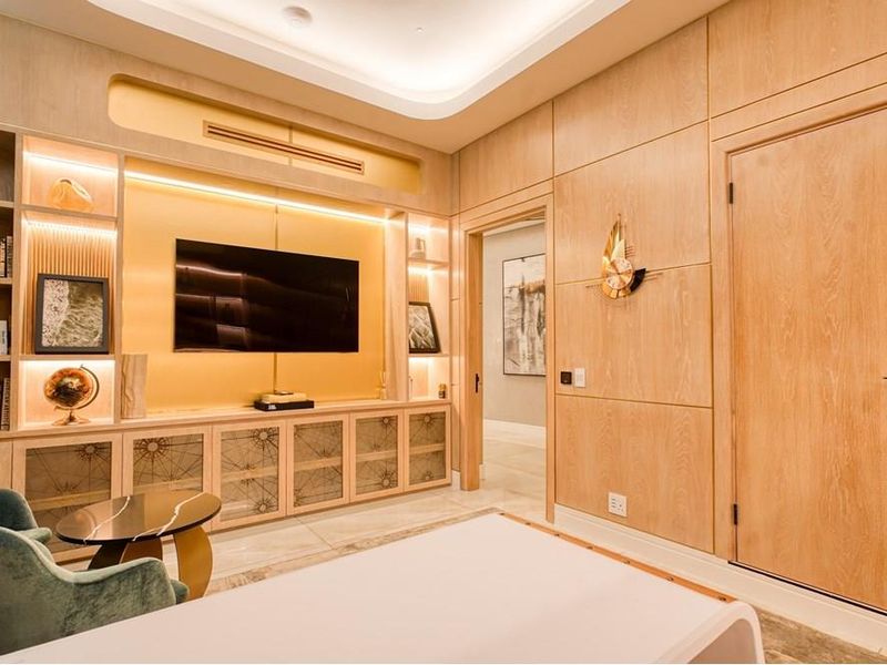 A sophisticated living room featuring custom light wood built-in cabinetry, integrated display shelving, recessed cove lighting, and high-quality marble flooring.