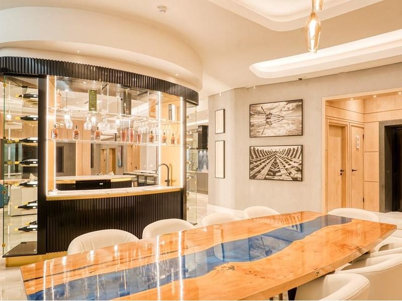 A sophisticated, modern bar area featuring a custom built-in counter, integrated wine display shelving, and elegant recessed ceiling lighting with high-end finishes.