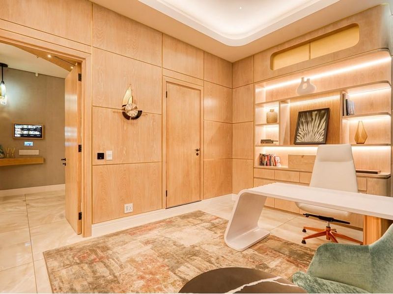 A sophisticated home office featuring custom wood veneer wall paneling, integrated shelving with ambient LED lighting, and high-quality tiled flooring.