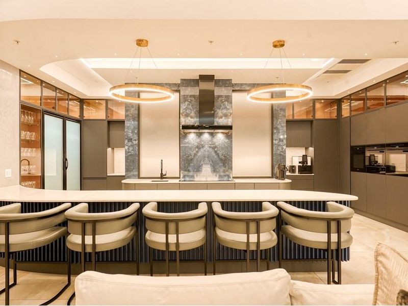 Modern luxury kitchen featuring high-end integrated appliances, stone countertops, custom cabinetry, and elegant pendant lighting in a spacious open-plan layout.