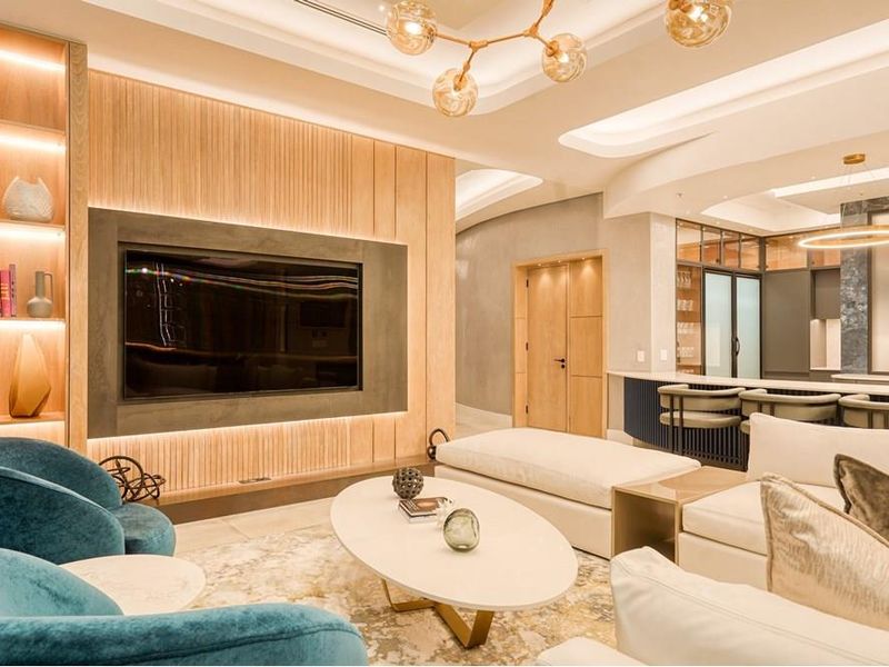 Luxurious open-plan living area featuring a custom media wall, integrated lighting, and a modern kitchen with a central island and premium finishes.