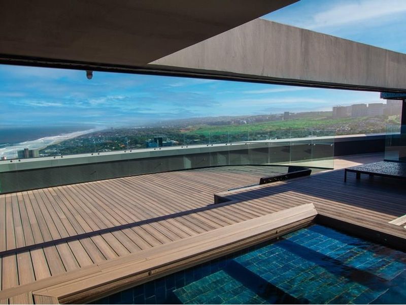 Spacious penthouse terrace featuring a modern swimming pool, timber decking, and a glass balustrade offering expansive coastal and city views.