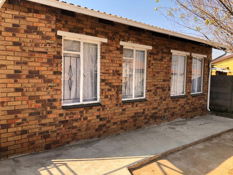 A side view of the property featuring a face brick exterior, white-framed windows with security bars, and a concrete walkway.