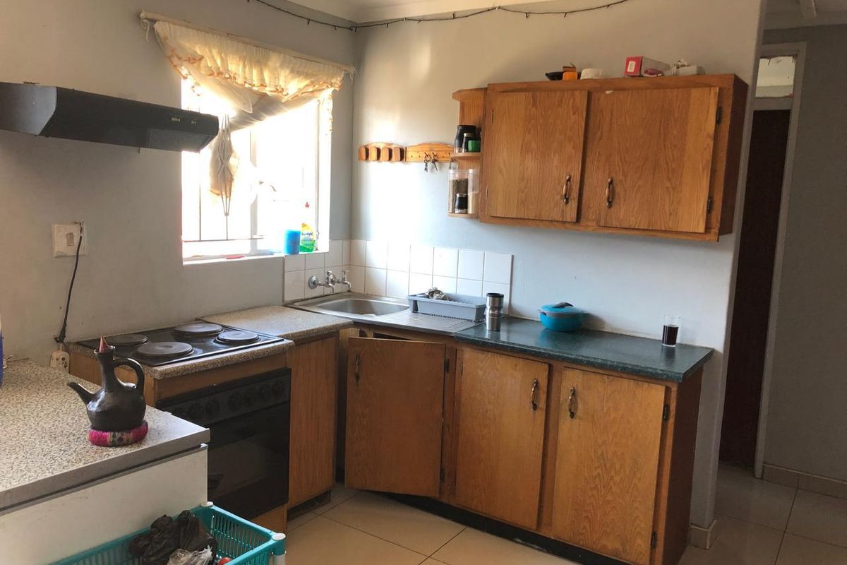A functional kitchen featuring wooden cabinetry, laminate countertops, a built-in electric stove with extractor fan, and tiled flooring.