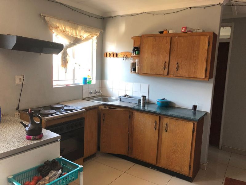 A functional kitchen featuring wooden cabinetry, laminate countertops, a built-in electric stove with extractor fan, and tiled flooring.
