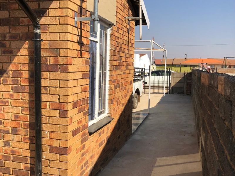 A side view of the property showing a face brick exterior, concrete pathway, and boundary wall.