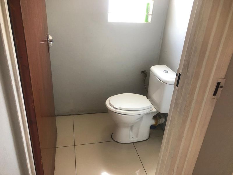 A small, functional bathroom featuring a standard toilet, tiled flooring, and a window, currently in need of cosmetic updates and finishing touches.