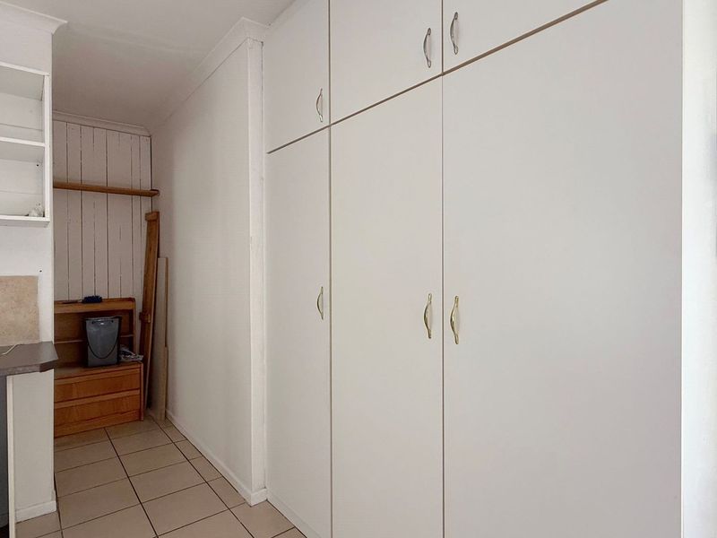A functional laundry area featuring extensive built-in white cabinetry for storage and durable tiled flooring.