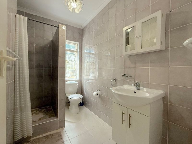 A functional bathroom featuring a walk-in shower, a white vanity with basin, a wall-mounted cabinet, and neutral floor-to-ceiling wall tiles.