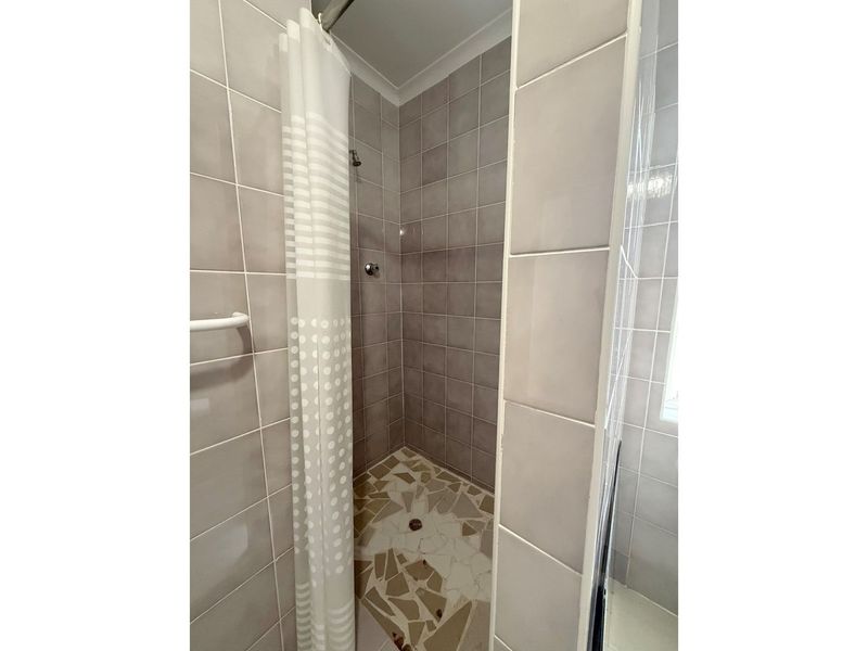 A compact shower stall featuring neutral wall tiling and a mosaic-style tiled floor, currently requiring maintenance on the floor surface.