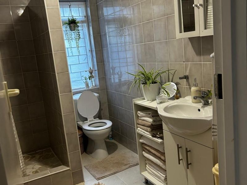 A well-maintained bathroom featuring a walk-in shower, vanity cabinet with basin, wall-mounted storage, and full-height wall tiling.
