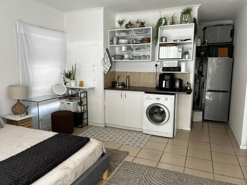 Compact kitchenette area featuring built-in cabinetry, tiled backsplash, integrated washing machine, and open shelving, requiring cosmetic updates to wall finishes.