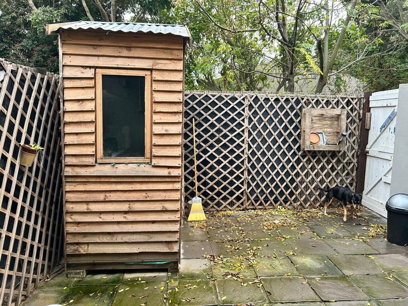 A rear garden area featuring a timber storage shed, paved patio flooring, and timber lattice fencing, providing a functional outdoor utility space.