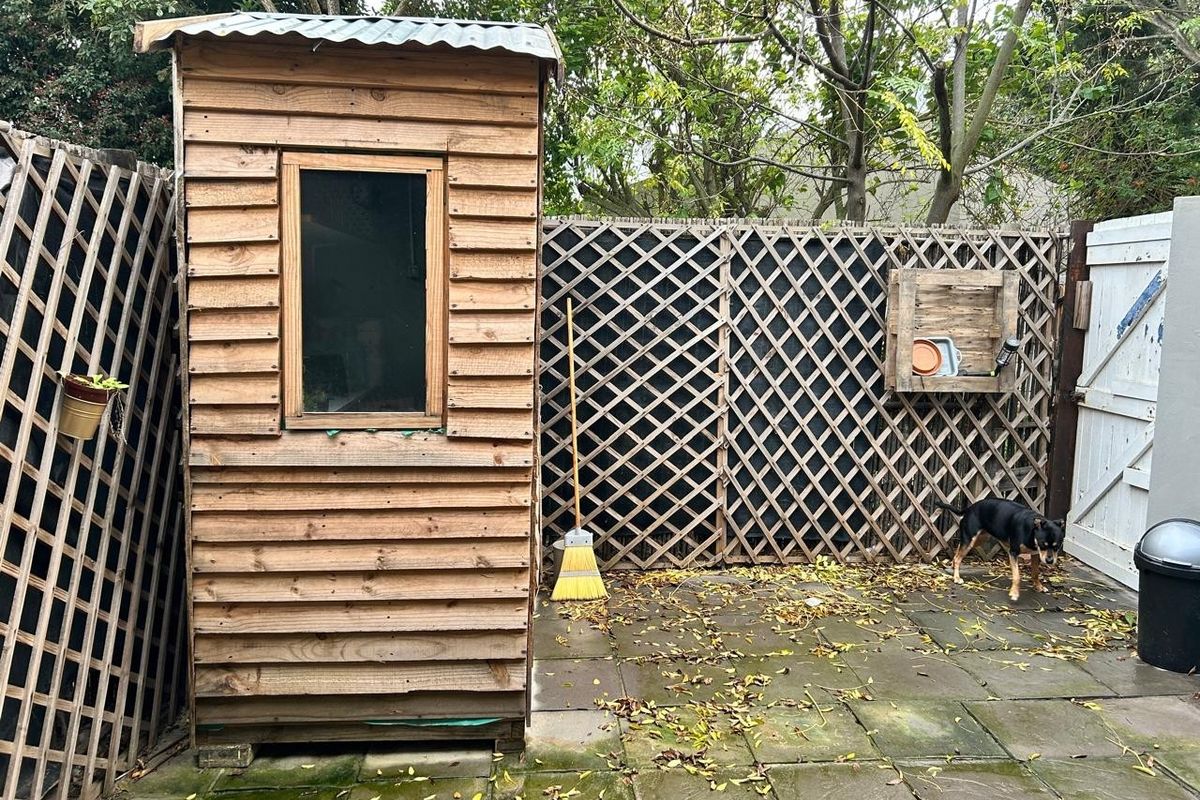 A rear garden area featuring a timber storage shed, paved patio flooring, and timber lattice fencing, providing a functional outdoor utility space.