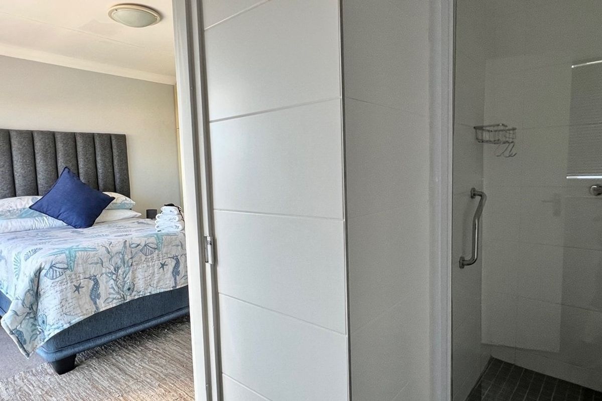 A view from a bathroom doorway looking into a bedroom, featuring a modern shower enclosure with a grab rail and a well-appointed sleeping area.
