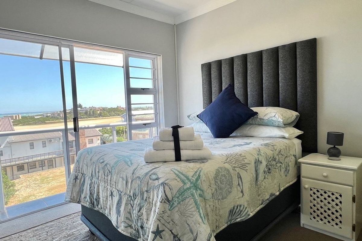 A bright bedroom featuring a large sliding glass door that opens to a balcony with scenic coastal views.