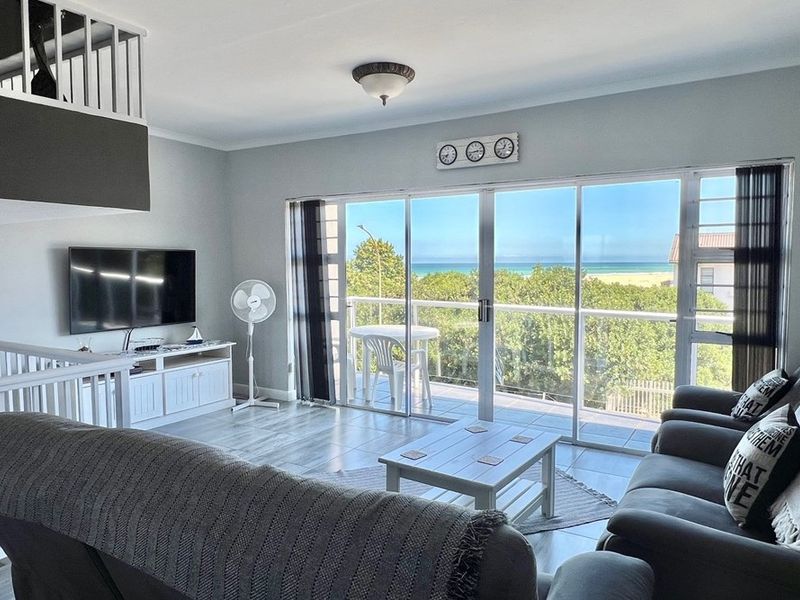 Bright open-plan living area featuring large sliding glass doors that open onto a balcony with scenic ocean views.