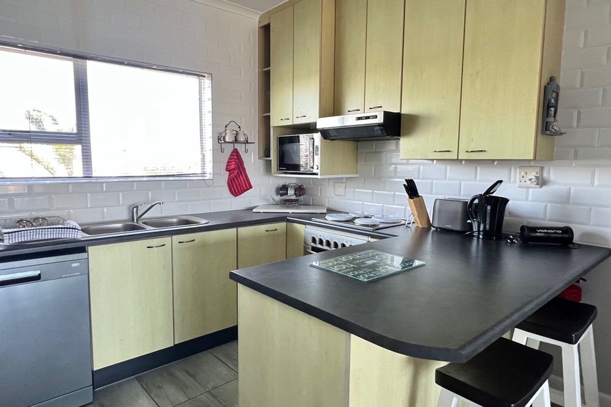 A functional kitchen featuring light-toned cabinetry, dark laminate countertops, subway tile backsplash, and integrated appliances including a stove and extractor fan.