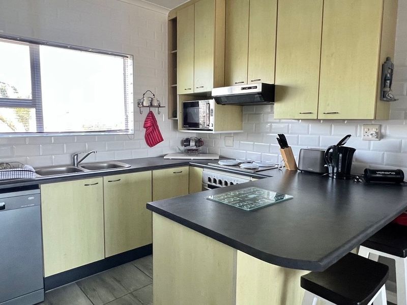 A functional kitchen featuring light-toned cabinetry, dark laminate countertops, subway tile backsplash, and integrated appliances including a stove and extractor fan.