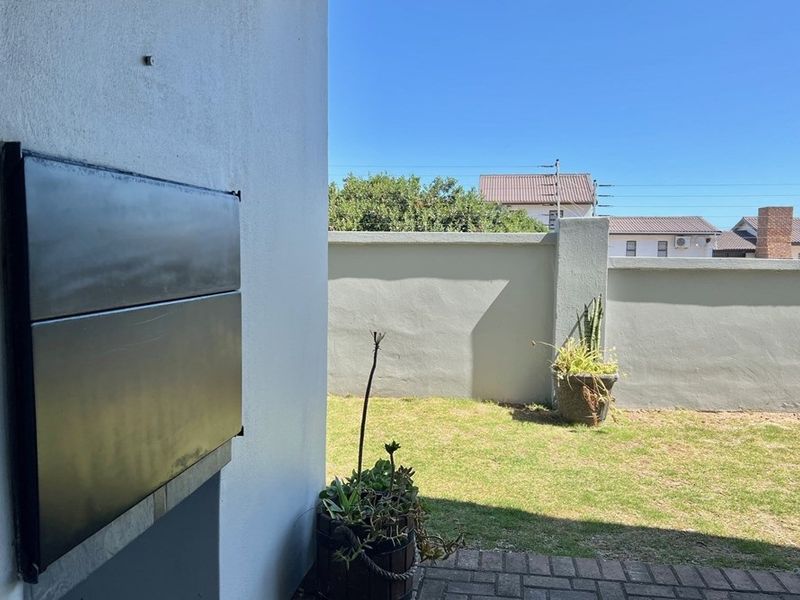 A private outdoor patio area featuring a built-in braai, overlooking a small, enclosed garden with a perimeter wall.