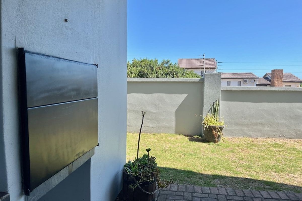 A private outdoor patio area featuring a built-in braai, overlooking a small, enclosed garden with a perimeter wall.