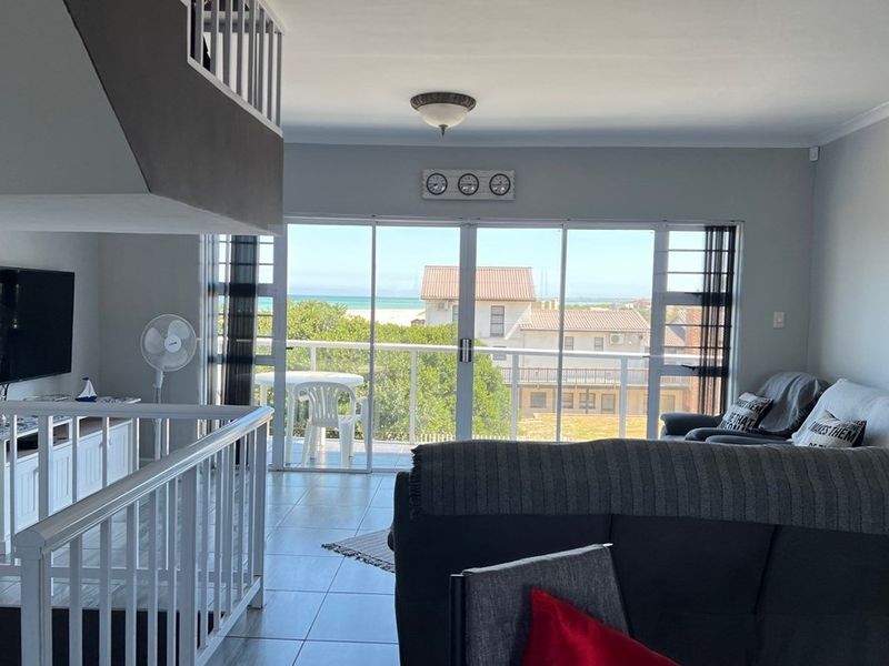 Open-plan living area featuring tiled flooring, a staircase with white balustrades, and large sliding glass doors opening onto a balcony with coastal views.