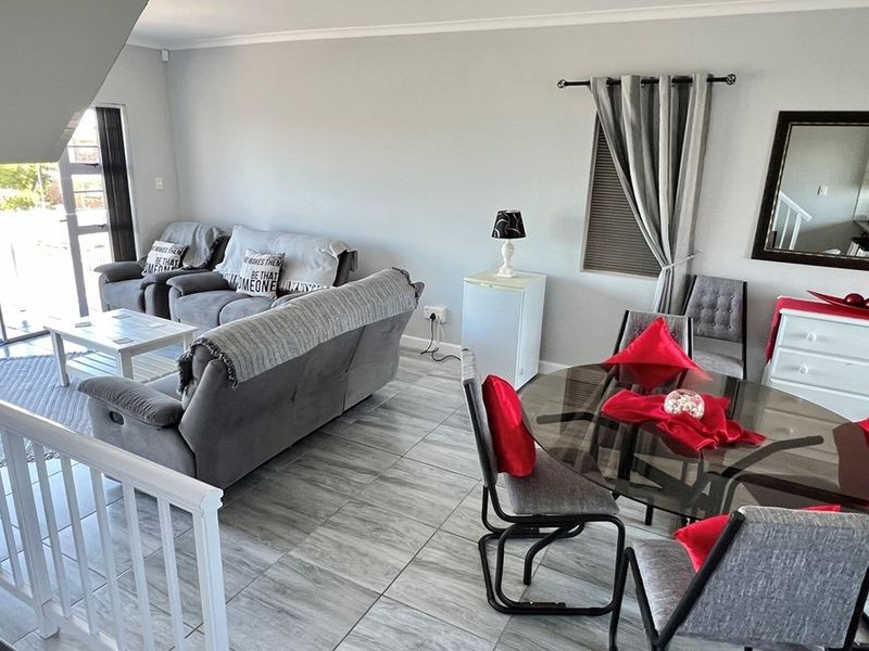 Open-plan living and dining area featuring neutral wall tones, modern grey floor tiles, and sliding glass doors leading to an outdoor space.