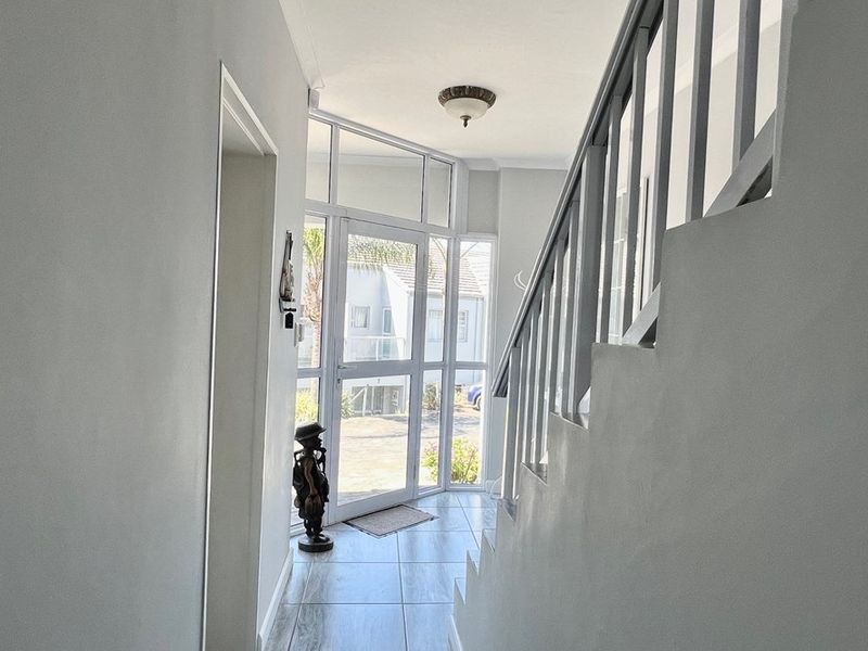 Bright entrance hallway featuring tiled flooring, a glass-paneled front door with sidelights, and a staircase with a painted wooden balustrade.