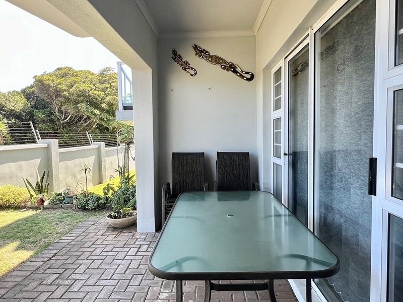 A covered patio area featuring paved flooring and sliding glass doors, providing direct access to the garden.