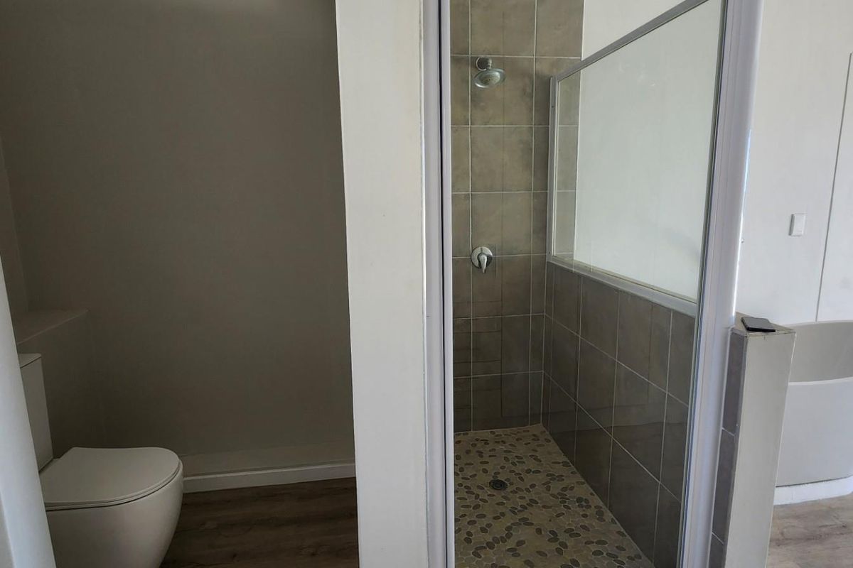 Modern bathroom featuring a walk-in shower with tiled walls, a separate toilet, and a freestanding bathtub on wood-look flooring.