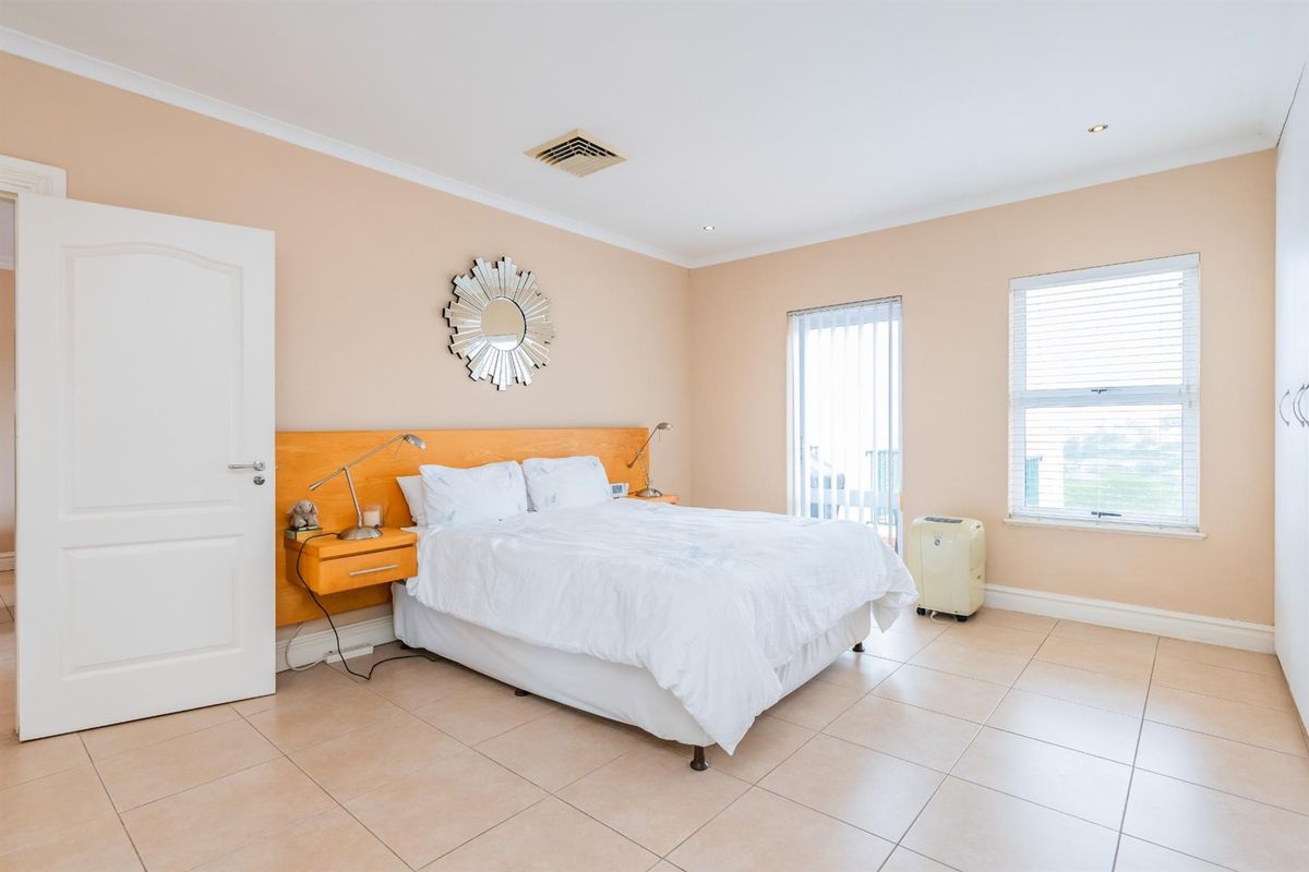 Spacious bedroom featuring neutral tiled flooring, built-in headboard with integrated lighting, and access to a private balcony through sliding glass doors.