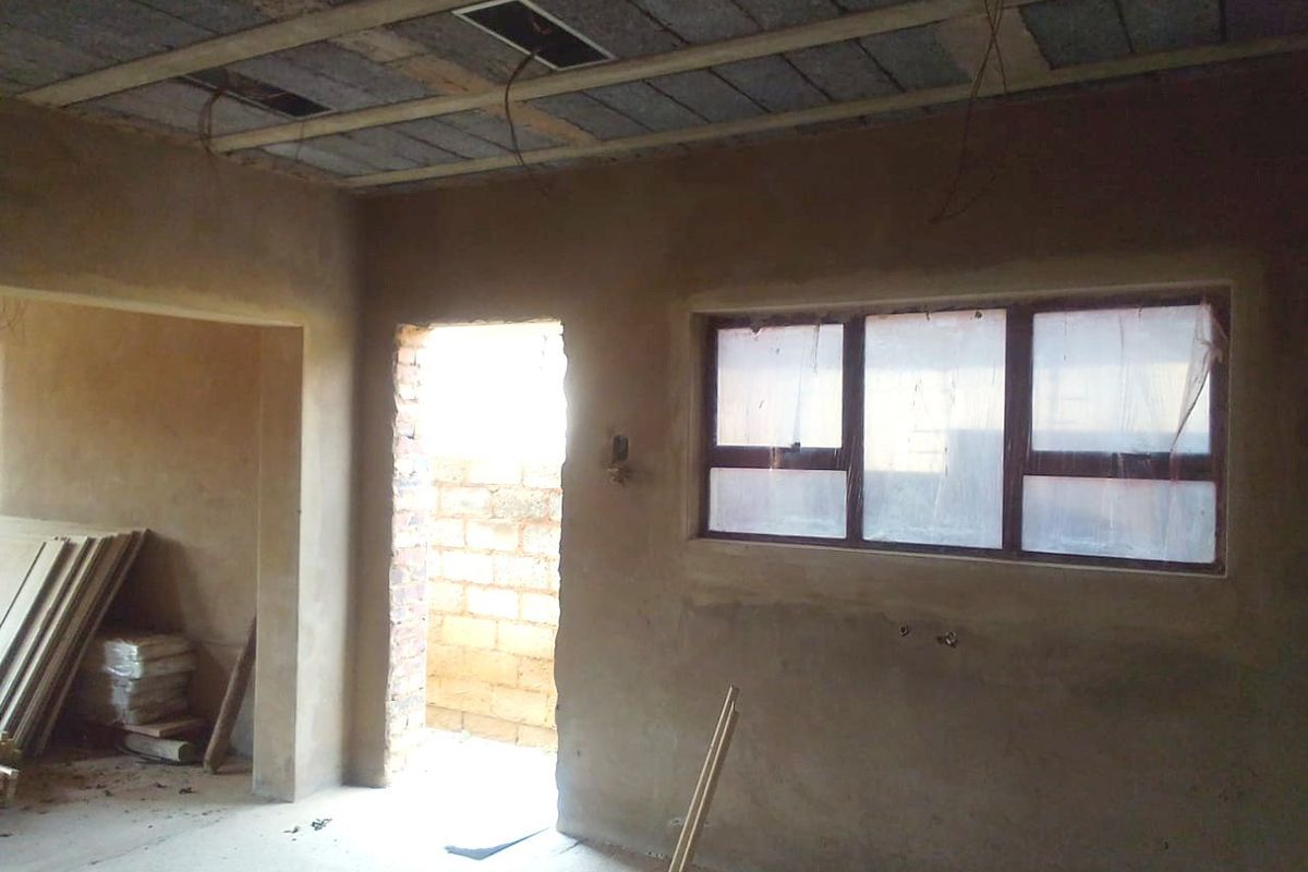An interior space currently under construction, featuring raw plaster walls, exposed ceiling joists, and an unfinished doorway leading to an exterior area.