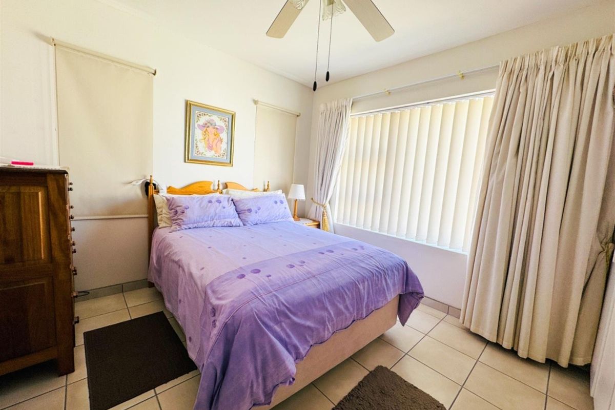A bedroom featuring tiled flooring, a ceiling fan, and large windows with vertical blinds and curtains.