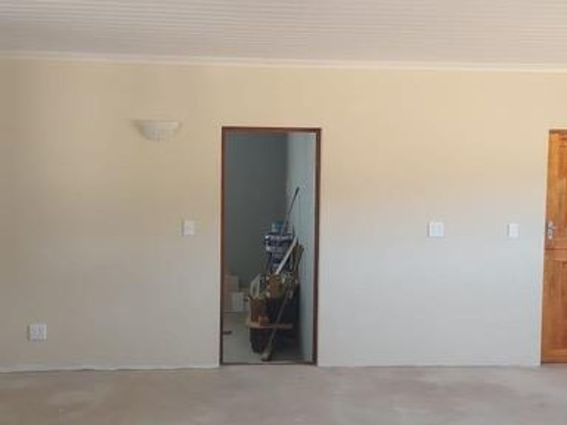 An interior view of a room featuring a wooden door, wall-mounted light fixtures, and an open doorway leading to an adjacent space.