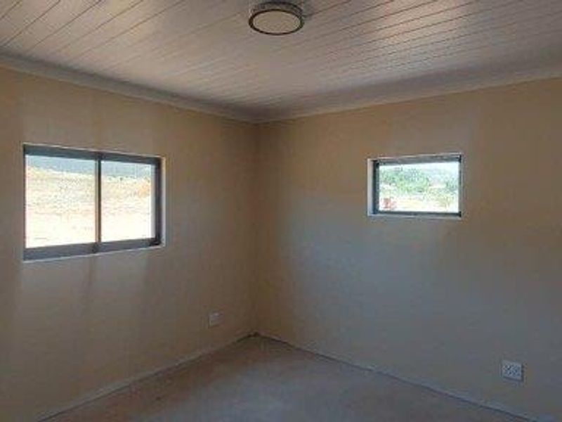 A clean, empty bedroom featuring neutral walls, a tongue-and-groove ceiling, and sliding windows providing natural light.