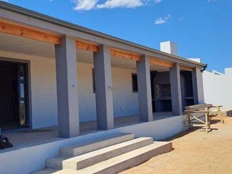 A spacious covered patio featuring concrete steps, structural pillars, and a built-in braai area, overlooking an expansive, undeveloped outdoor space.