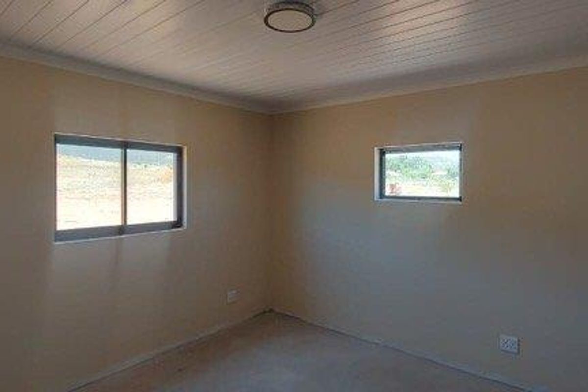 A clean, empty bedroom featuring neutral walls, a tongue-and-groove ceiling, and sliding windows providing natural light.