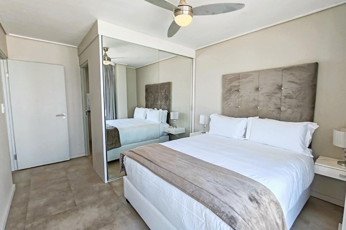 A well-maintained bedroom featuring tiled flooring, a ceiling fan, and large built-in mirrored cupboards providing ample storage space.