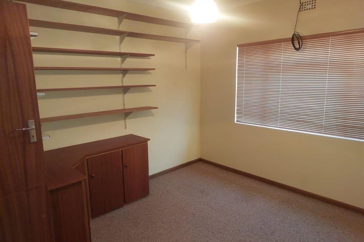 A functional bedroom or office space featuring built-in wooden cabinetry, wall-mounted shelving, and venetian blinds.