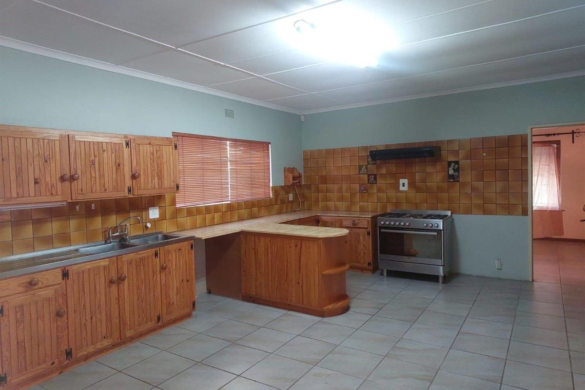Spacious kitchen featuring wooden cabinetry, tiled flooring, a built-in stove with extractor fan, and a functional layout with ample counter space.